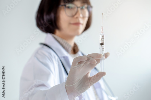 The female doctor holds a syringe with liquid inside.