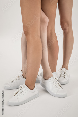 Three girls models with long tanned legs in white shoes shot in studio on white background 