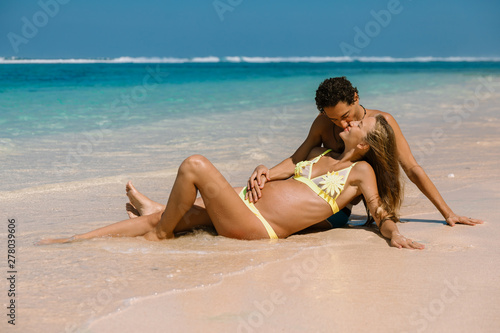Happy pregnant woman with husband expecting baby at tropical beach