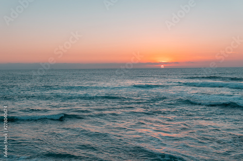 Sunset above sea or ocean. Wavy surface of water. Horizon line. Teal and orange colors concept