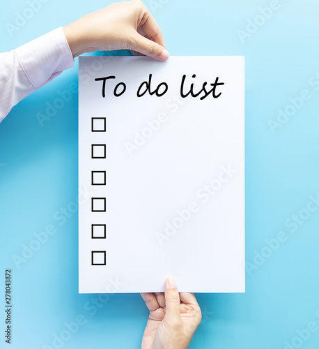 hand holding paper with to do list and checkbox by hand drawn text isolated on blue background, planning and design concept