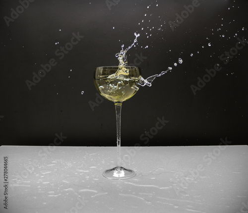 Water in glass with some splash around it. White table, black background.
