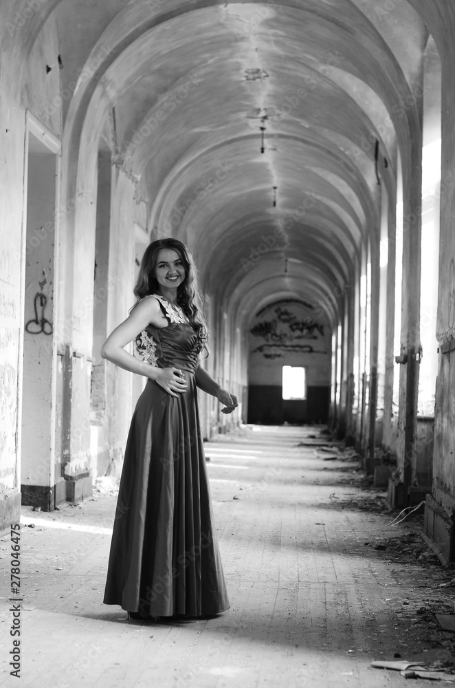 Naklejka premium Young beautiful short hair blonde woman in black climbing the stairs, black and white photo. Side view of elegant romantic mysterious lady with movie star look in interior with bricks walls