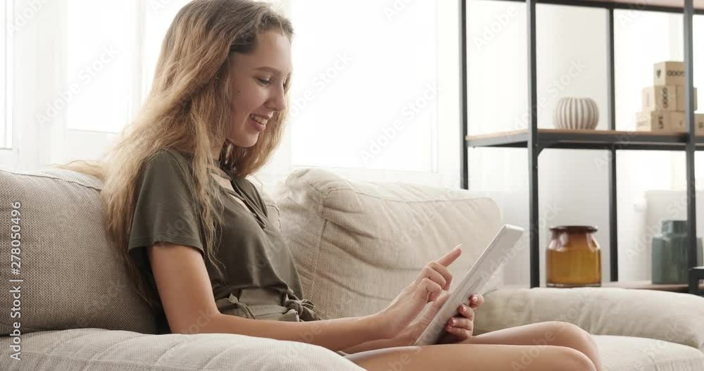 Happy teenage girl using digital tablet on sofa at home Happy teenage girl using digital tablet on sofa at home