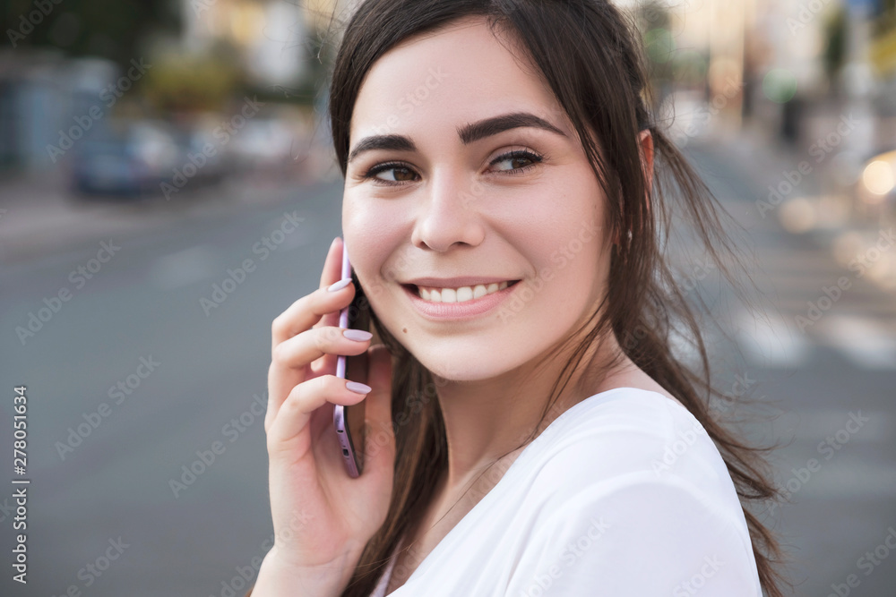 Beautiful brunette business woman in white skirt and grey suit trousers talking on a mobile phone in her hands outdoors. European city on background. copy space Beautiful brunette business woman in white skirt and grey suit trousers talking on a mobile phone in her hands outdoors. European city on background. copy space