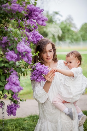 Beautiful young mother and daughter near the blossoming lilac. Spring.