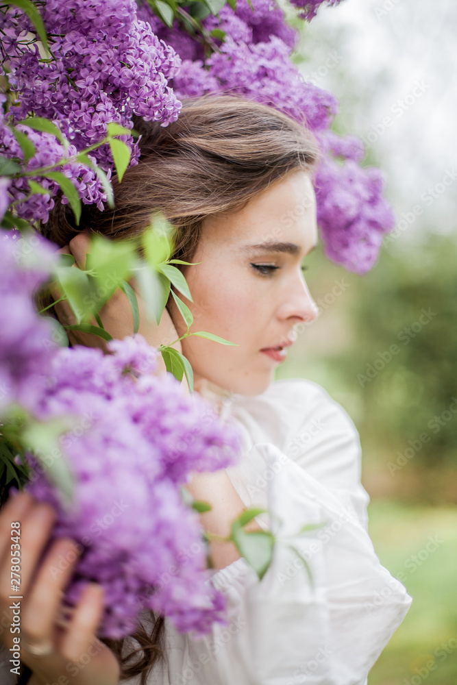 Fototapeta premium Portrait of a beautiful young woman near the blossoming lilac. Spring.