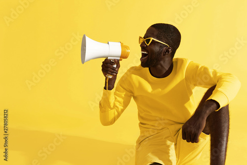 Man screaming in megaphone on yellow background portrait