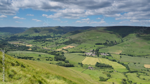 View across Edale valley and Kinder Scout plateau in the background and white clouds against a blue sky, Peak District National Park, UK