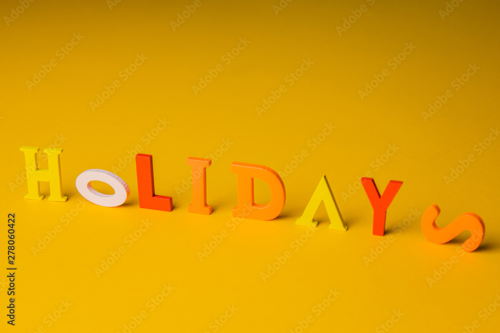 the inscription holidays from colorful bright wooden letters lie on a bright yellow background top view copy space the inscription holidays from colorful bright wooden letters lie on a bright yellow background top view copy space