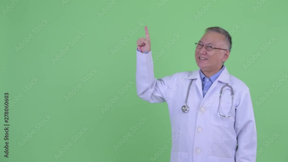 Happy mature Japanese man doctor pointing up and looking excited Happy mature Japanese man doctor pointing up and looking excited