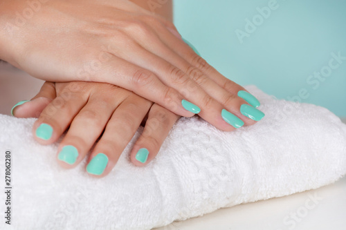 Young girl hands with a turquoise color nails polish on a white towel on desk isolated on soft blue background in studio. Manicure and beauty concept. Close up  selective focus