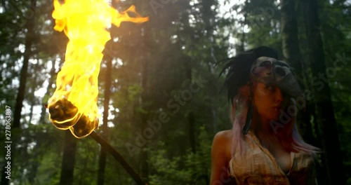 menacing female shaman is holding flaming torch in hand in forest, medium shot photo