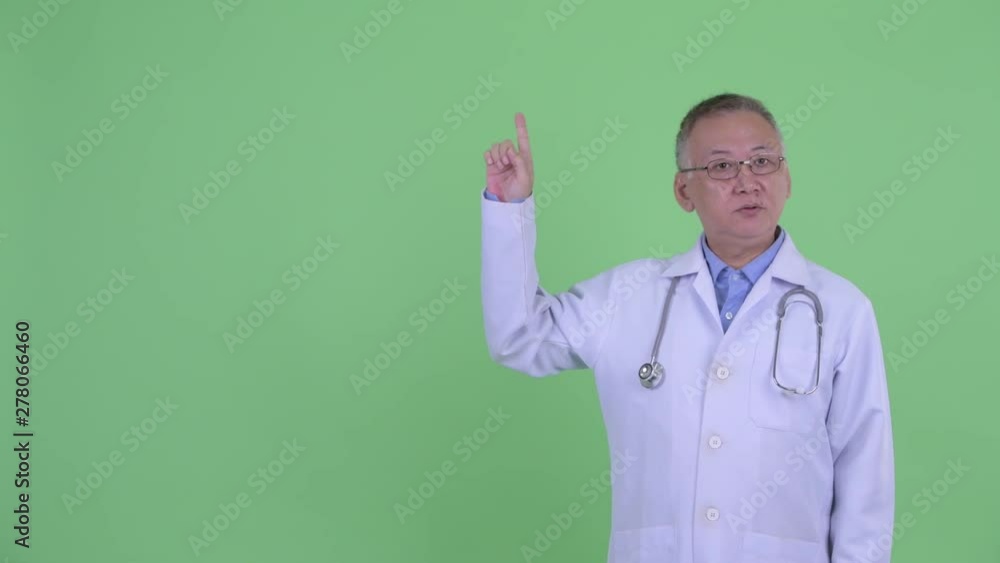 Happy mature Japanese man doctor talking while pointing up Happy mature Japanese man doctor talking while pointing up