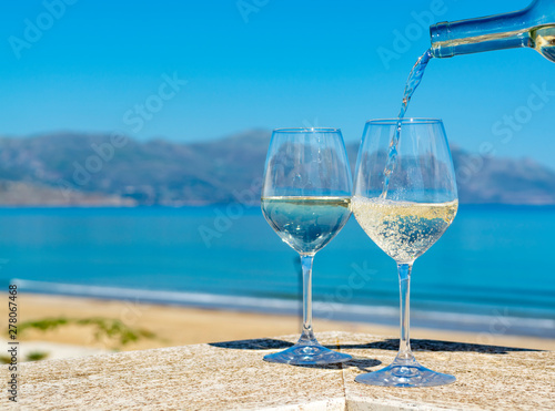 Waiter pouring white wine in wine glasses on outdoor terrace witn blue sea and mountains view on background