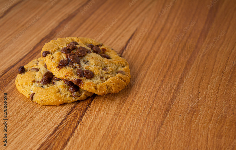 Two homemade cookies with chocolate pieces on a light wood table Two homemade cookies with chocolate pieces on a light wood table