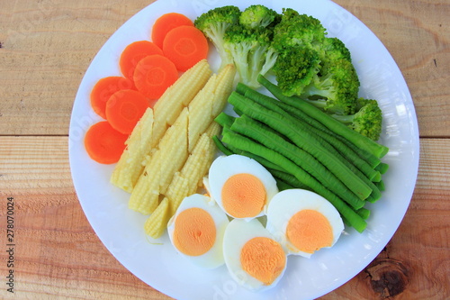 Fresh green broccoli,carrot,Lentils,Baby corn,and egg in white disc on the wood table, healthy or vegetarian food concept Top view.