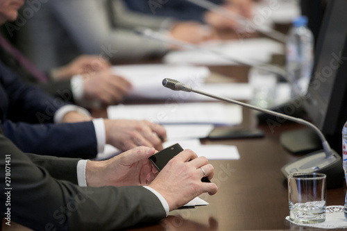Billede på lærred A politician or businessman in a suit sits at a polished wooden table in front of a microphone during a discussion, duty, or presentation