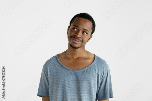 Beautiful male half-length portrait isolated on white studio background. Young emotional african-american man in blue shirt. Facial expression, human emotions, ad concept. Smiling, looking at side.