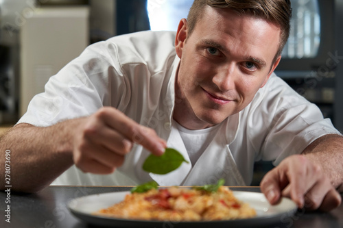 Portrait Of Male Chef Garnishing Plate Of Food In Professional Kitchen