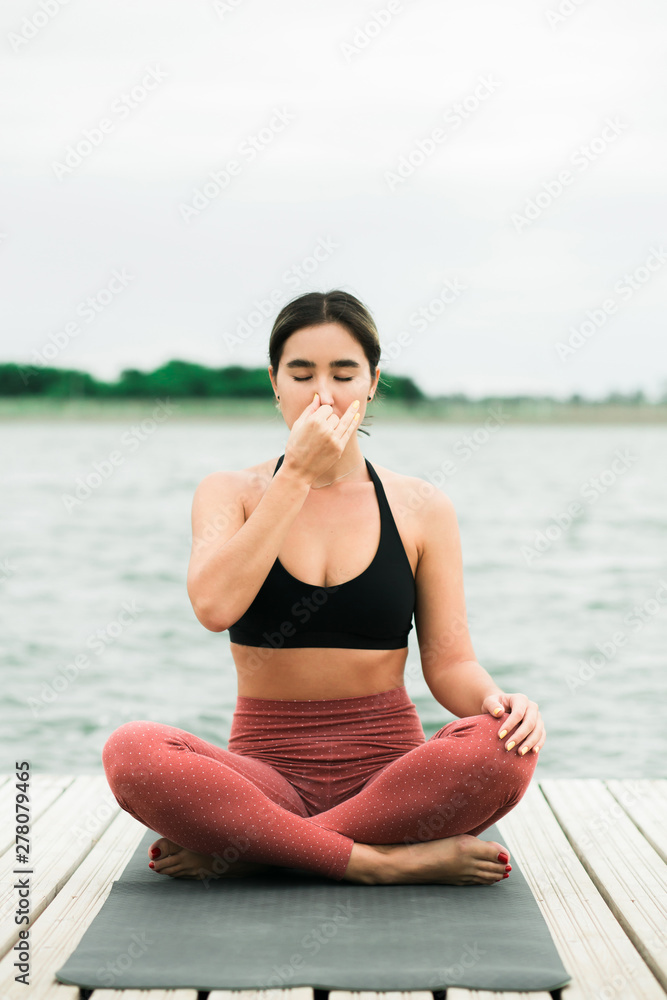 Fototapeta premium Asian young girl doing meditation outdoors on the pier by the lake.