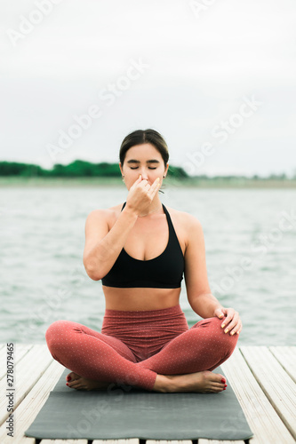 Asian young girl doing meditation outdoors on the pier by the lake.