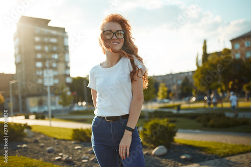 Portraits of a charming red-haired girl with a cute face. Girl posing for the camera in the city center. She has a wonderful mood and a lovely smile