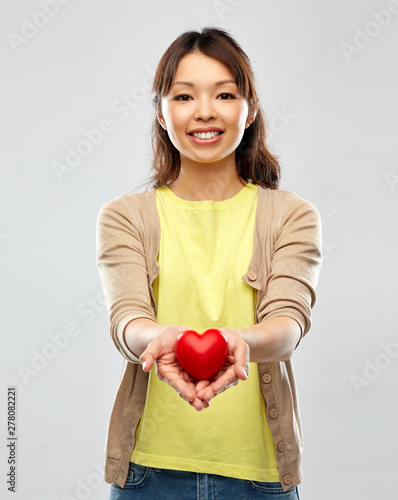 love, valentine's day and charity concept - happy asian young woman holding red heart over grey background