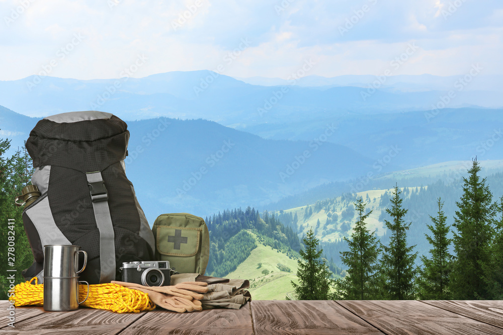 Set with different camping equipment on wooden table in mountains, space for text Set with different camping equipment on wooden table in mountains, space for text
