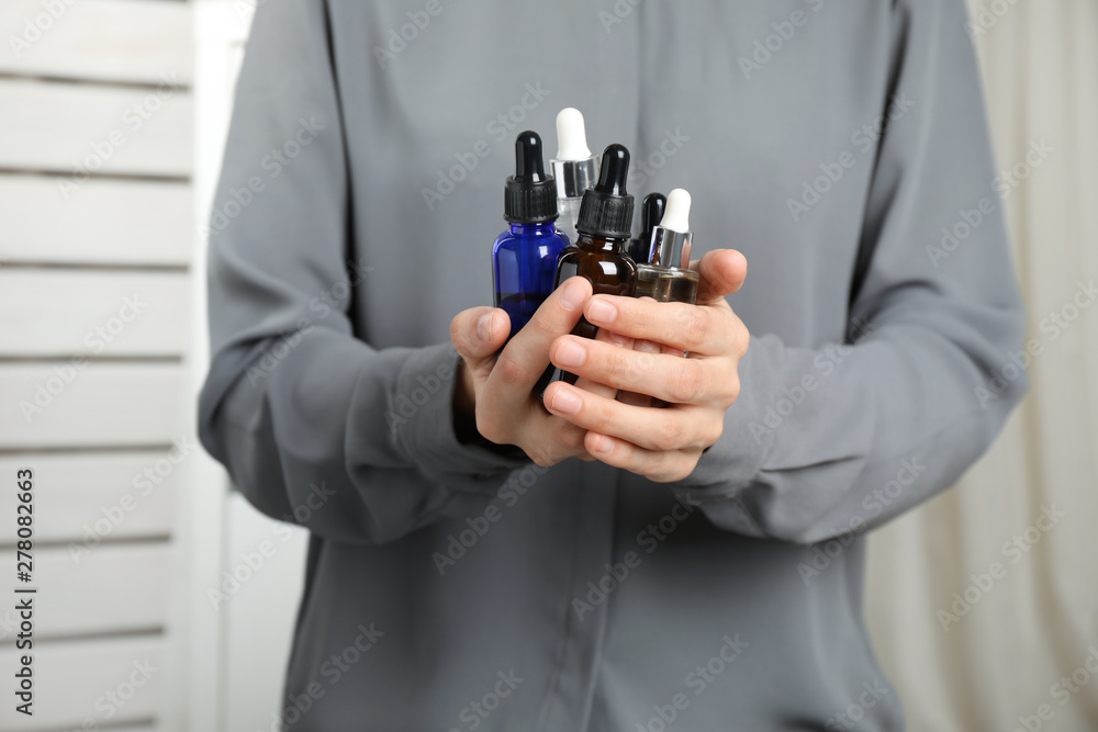Woman holding bottles with essential oils on blurred background, closeup Woman holding bottles with essential oils on blurred background, closeup