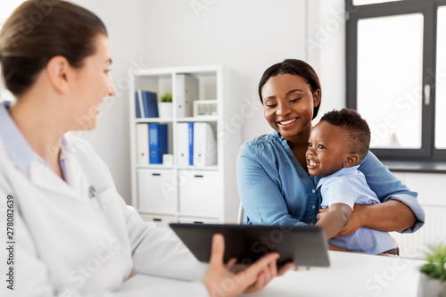 medicine, healthcare and pediatry concept - african american mother with baby son and caucasian doctor with tablet computer at clinic