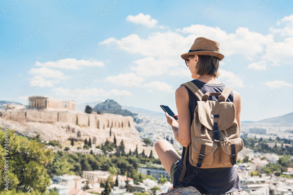 Young woman using smart phone in Athens with Acropolis at the background. Traveler girl enjoying vacation in Greece. Summer holidays, vacations, travel, tourism, technology concept. - obrazy, fototapety, plakaty 