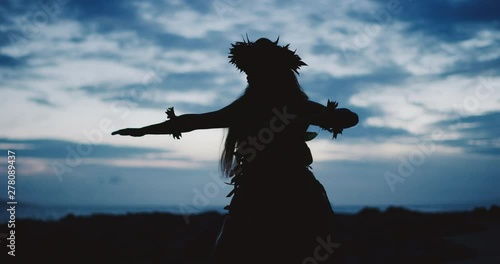 Silhouette of a traditional Hawaiian hula dancer woman dancing on a rugged island landscape at dusk in slow motion with an ocean background photo