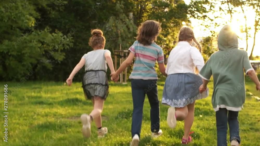 Happy children. Four classmates hugged each other and ran into the distance against the backdrop of green trees and sunset. School friendship, back to school, lens flare Happy children. Four classmates hugged each other and ran into the distance against the backdrop of green trees and sunset. School friendship, back to school, lens flare
