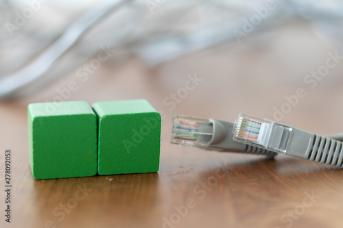 Two green wooden blocks with copyspace on the front beside grey lan cable on wooden table 