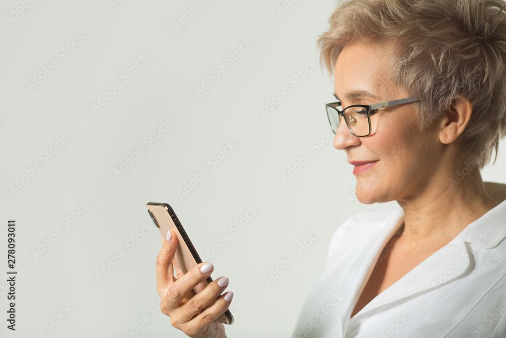 portrait of an adult woman with a short haircut wearing glasses in a white jacket on a white background with a phone in her hand