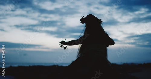 Silhouette of a traditional Hawaiian hula dancer woman dancing on a rugged island landscape at dusk in slow motion with an ocean background photo