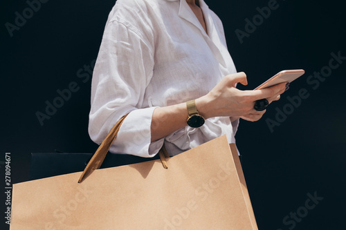 Unrecognisable cropped woman holding shopping bags and typing on her smartphone.