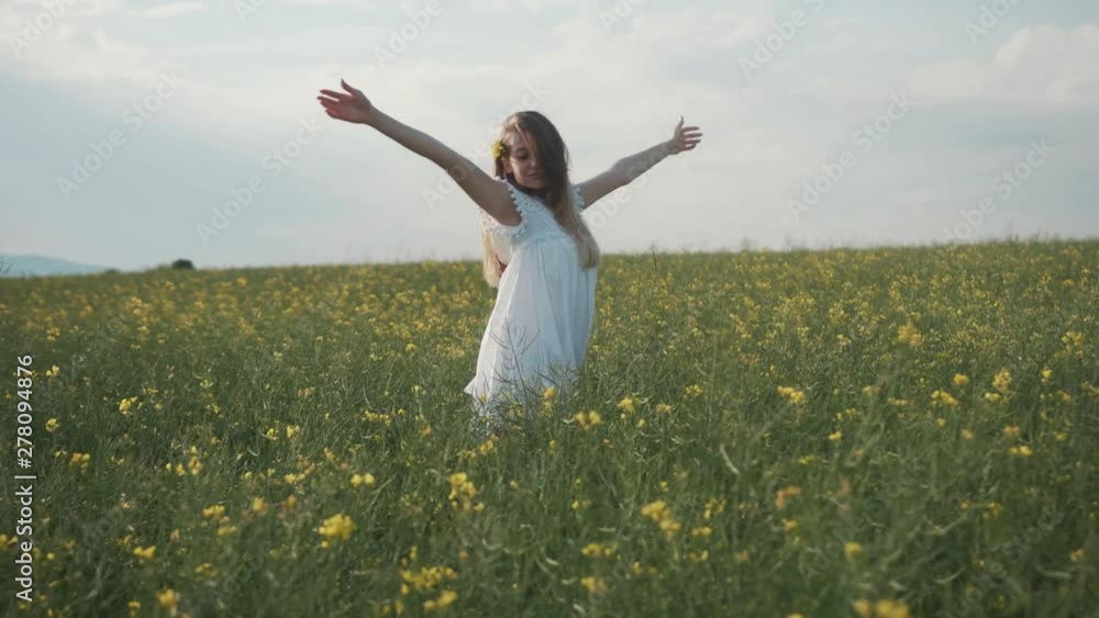 Cute young woman in a beautiful dress pleasure in a blooming yellow field turning around in place flower feel happy smile freedom meadow green landscape sunlight model close up slow motion Cute young woman in a beautiful dress pleasure in a blooming yellow field turning around in place flower feel happy smile freedom meadow green landscape sunlight model close up slow motion