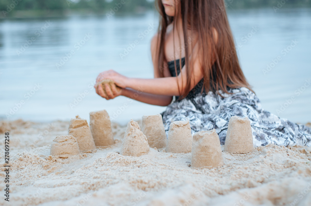 Little girl with long hair in summer dress playing with sand on the beach Little girl with long hair in summer dress playing with sand on the beach