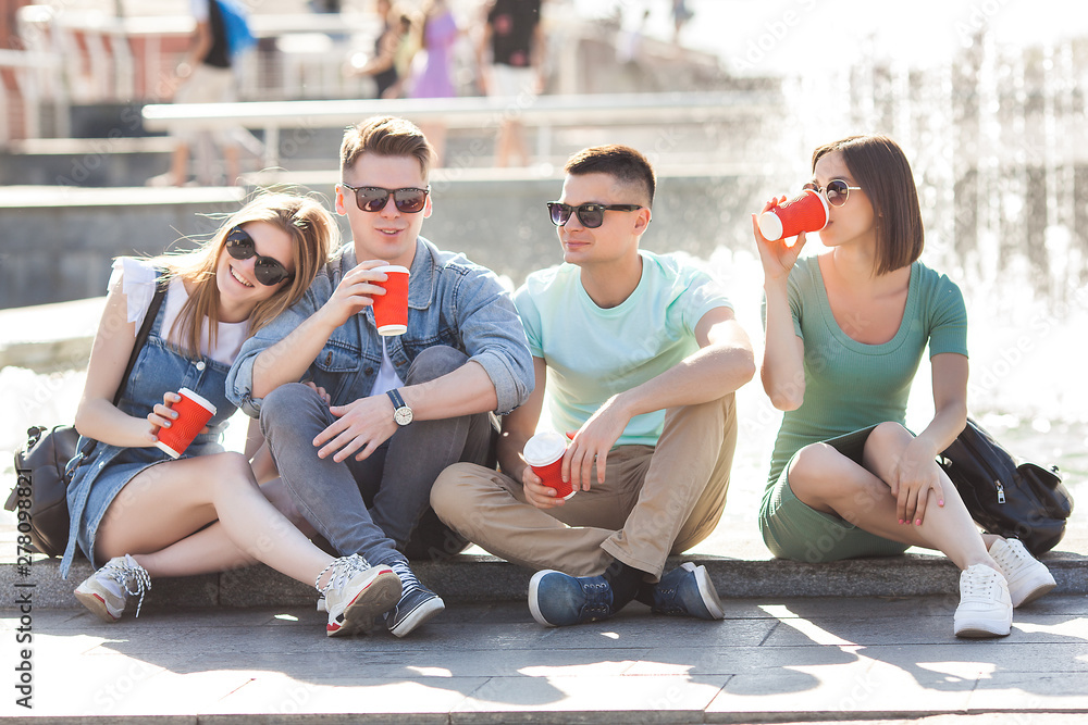 Fototapeta premium Group of young people near the fountain drinking coffee and having fun. friends relaxing outdoors.