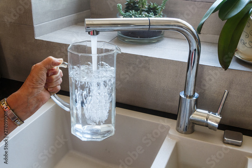 To fill a glass jug with tap water at the sink in a kitchen photo