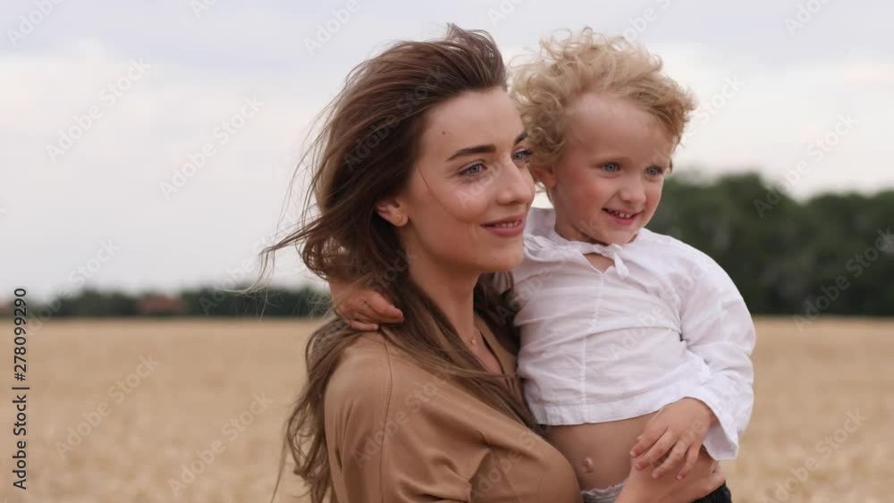 Young cute mother with curly child boy son hugging and spinning together walking in wheat field countryside nature Young cute mother with curly child boy son hugging and spinning together walking in wheat field countryside nature