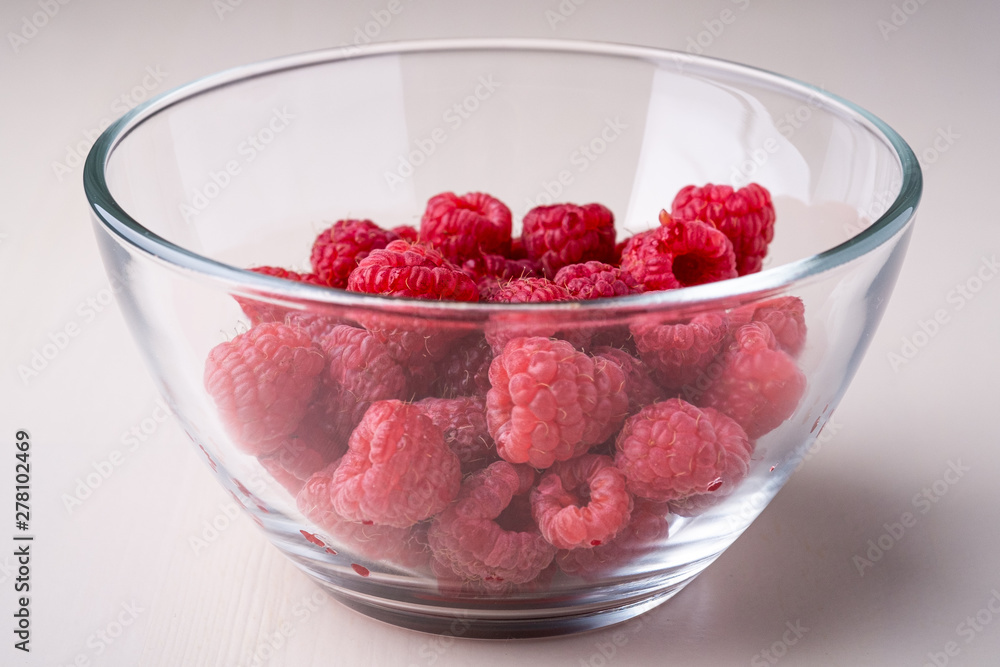 Raspberry red berries in transparent glass bowl plate tasty sweet bright on white background copy space macro Raspberry red berries in transparent glass bowl plate tasty sweet bright on white background copy space macro