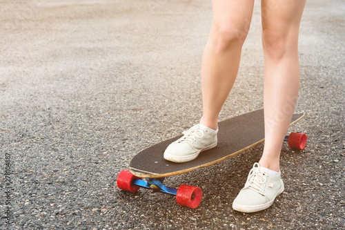 Close-up of female legs in rag sneakers on a longboard on the background of asphalt at sunset. Big skateboard with girl legs. Youth leisure concept