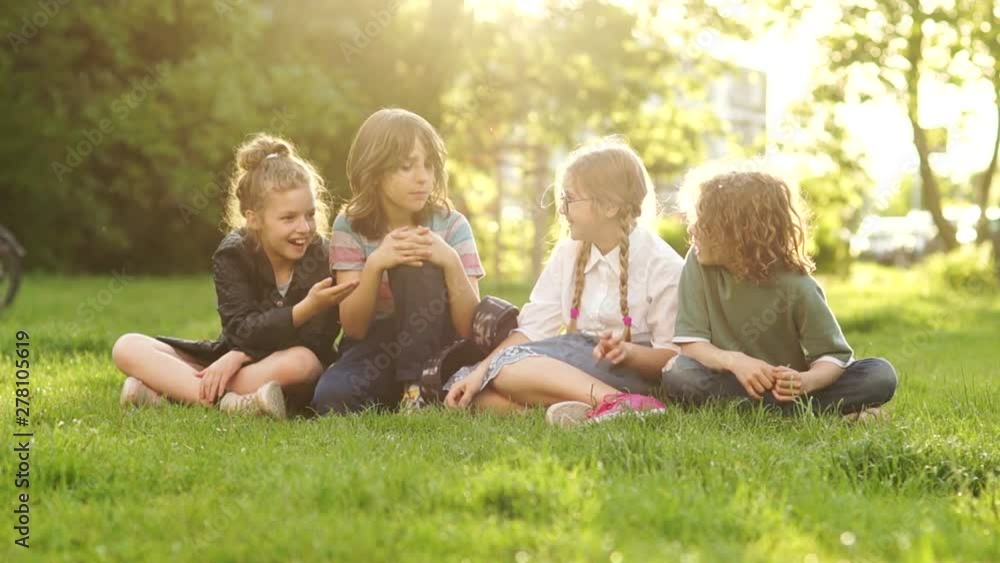 Back to school, students after school. Cheerful and friendly classmates chatting while sitting on the grass in the park during a school break Back to school, students after school. Cheerful and friendly classmates chatting while sitting on the grass in the park during a school break
