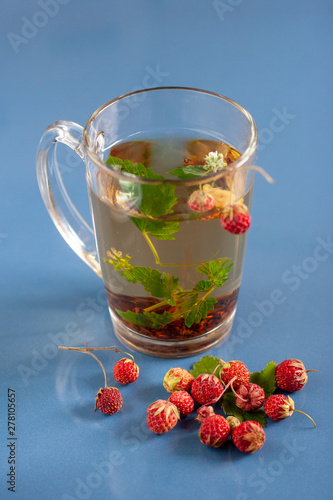 Still life of a mug of herbal tea on blue ceramic tiles with dust texture and reflection. Near scattered strawberries. Focus on the bottom berries. Selective focus. photo