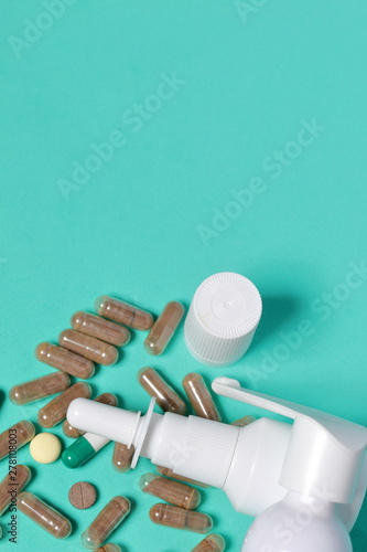 Gelatin pills and tablets of different colors. Sprays of oral and nasal sprays. Medicines scattered on the background of coral color.
