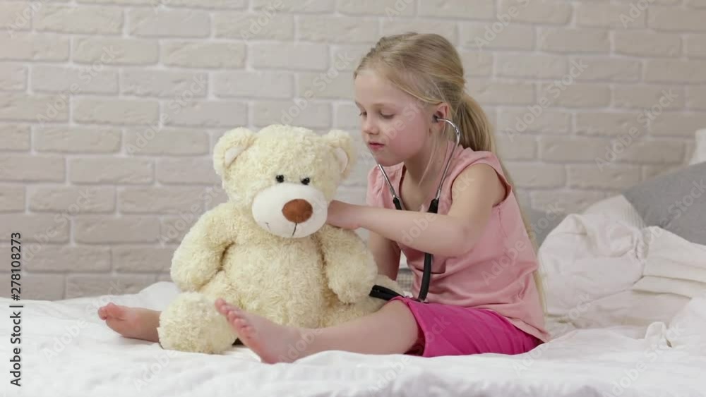cute child girl playing doctor with teddy bear at home. girl listens a stethoscope to toy. cute child girl playing doctor with teddy bear at home. girl listens a stethoscope to toy.