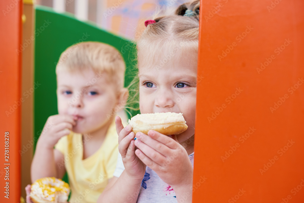 Cute toddler boy and girl is eating donuts outdoor. children is having fun with cakes. Tasty food for kids. Funny time at playground with sweet food. Bright and stylish kids. Cute toddler boy and girl is eating donuts outdoor. children is having fun with cakes. Tasty food for kids. Funny time at playground with sweet food. Bright and stylish kids.